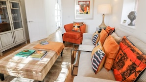 Ein Wohnzimmer mit Sofa, Sessel, Hocker, einem Schrank und einem gerahmten Bild an der Wand.