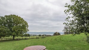 A picnic table in a grassy field with trees and a view of a body of water in the distance.