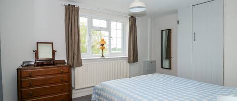 A bedroom with a bed, dresser, window, radiator, and a mirror.