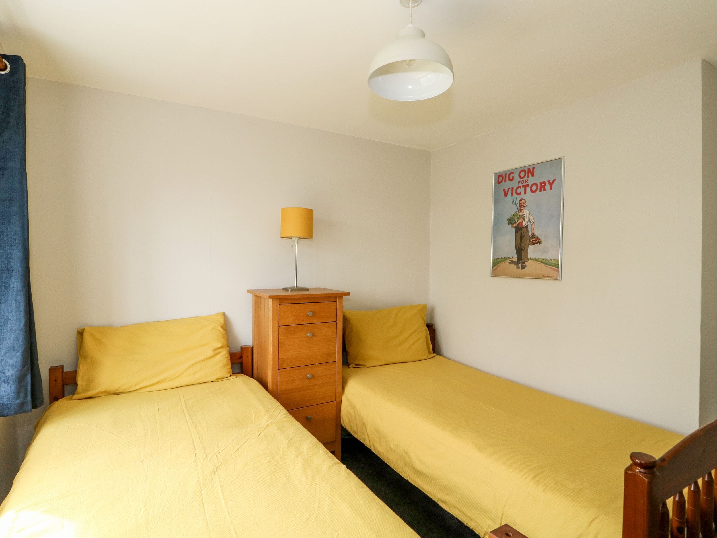 A bedroom with two single beds, a wooden dresser, a lamp, and a poster on the wall.