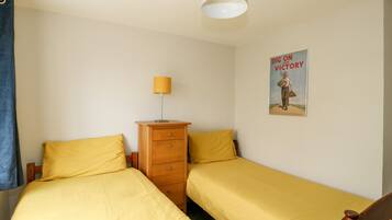 A bedroom with two single beds, a wooden dresser, a lamp, and a poster on the wall.
