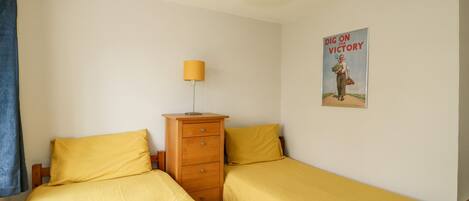 A bedroom with two single beds, a wooden dresser, a lamp, and a poster on the wall.