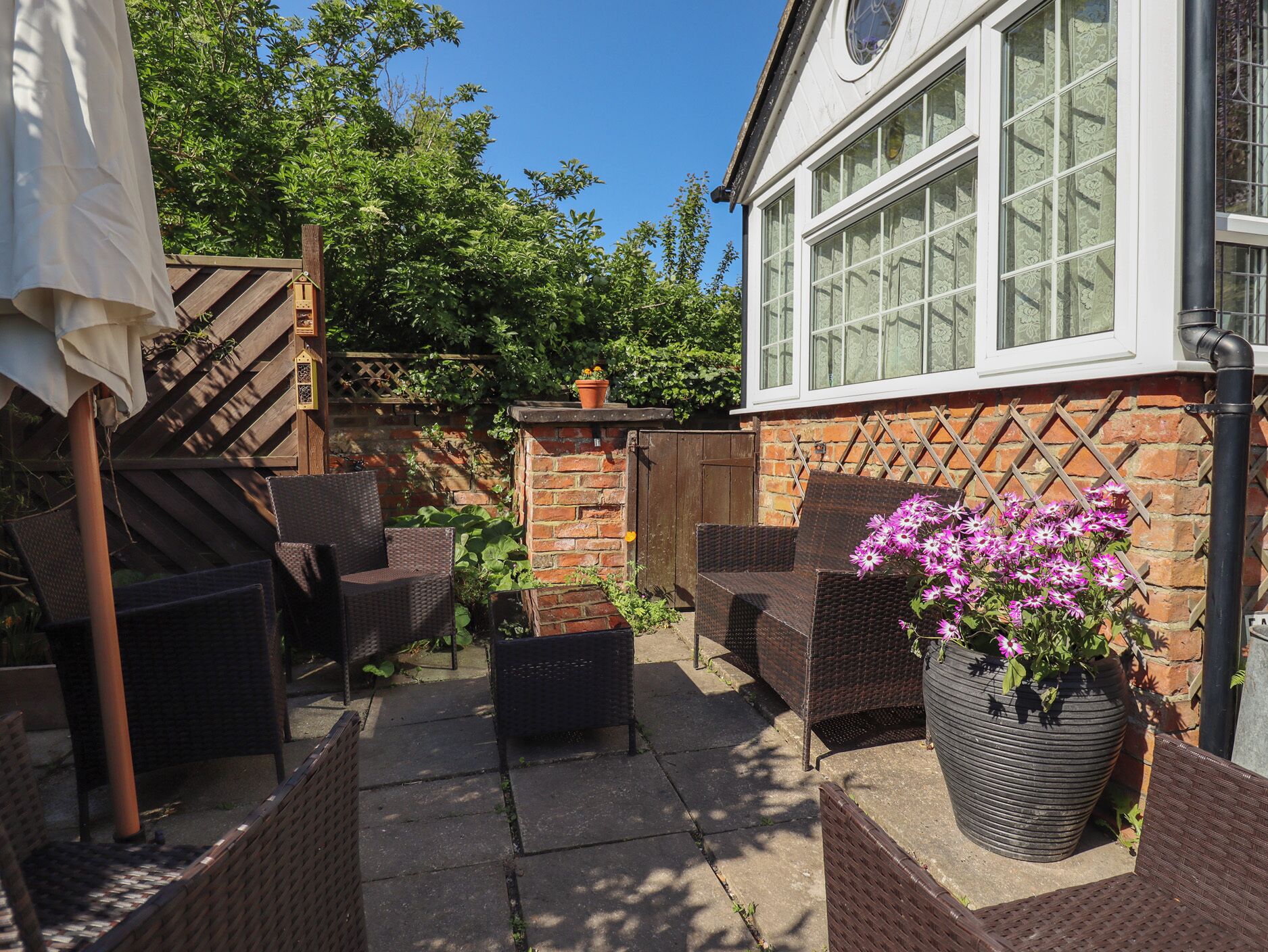 A patio area with wicker furniture, a potted plant with pink flowers, and a brick wall.