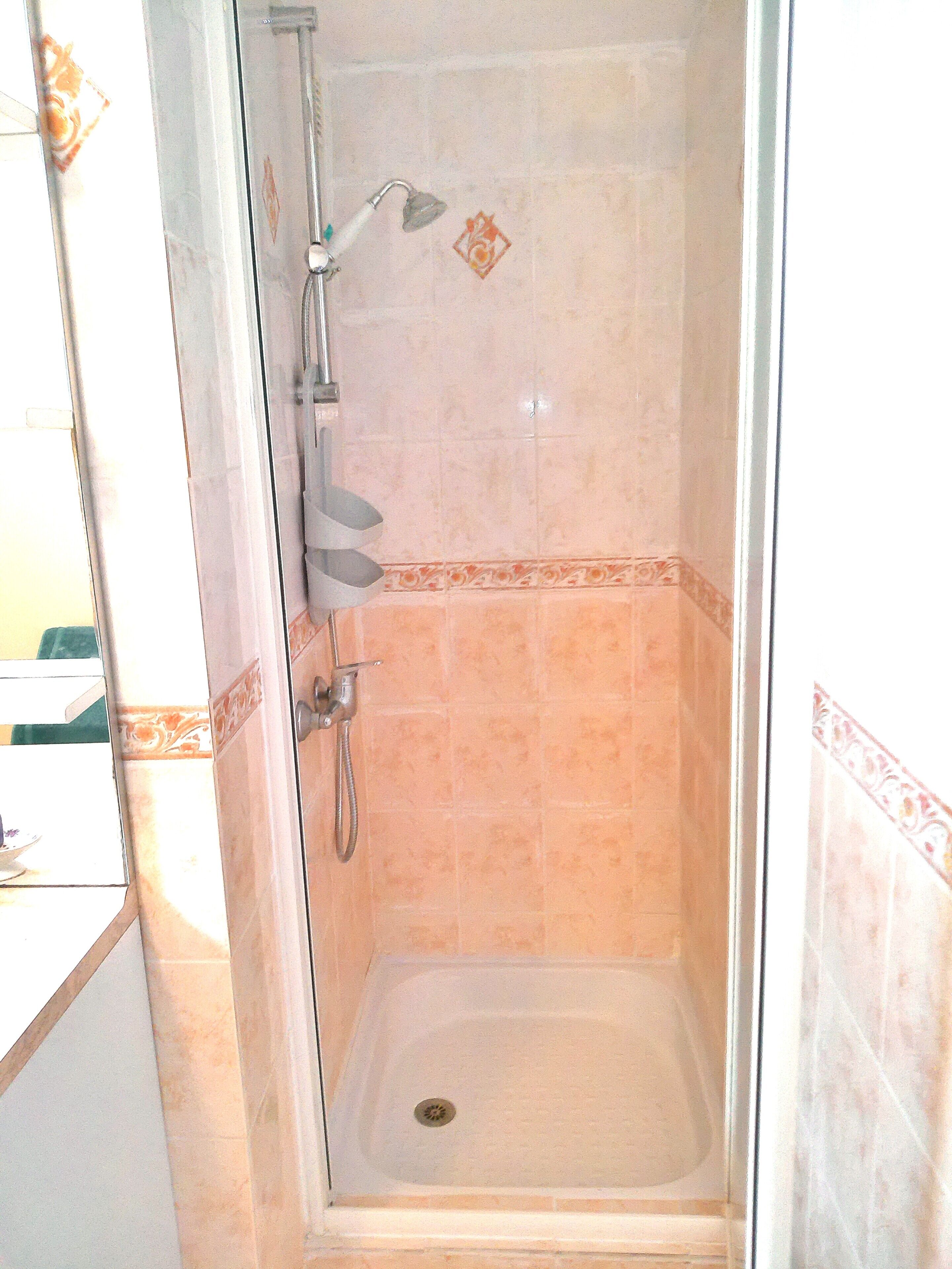 Une douche avec une porte en verre, un pommeau de douche et un drain.