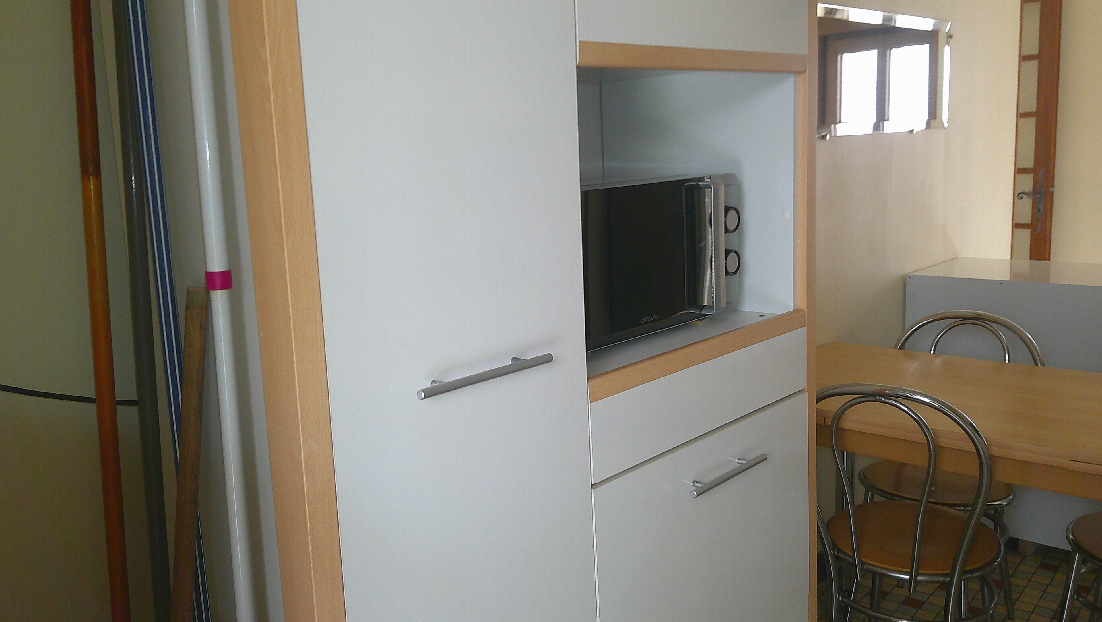 A compact kitchen with a microwave, a small refrigerator, and a dining area with metal chairs.