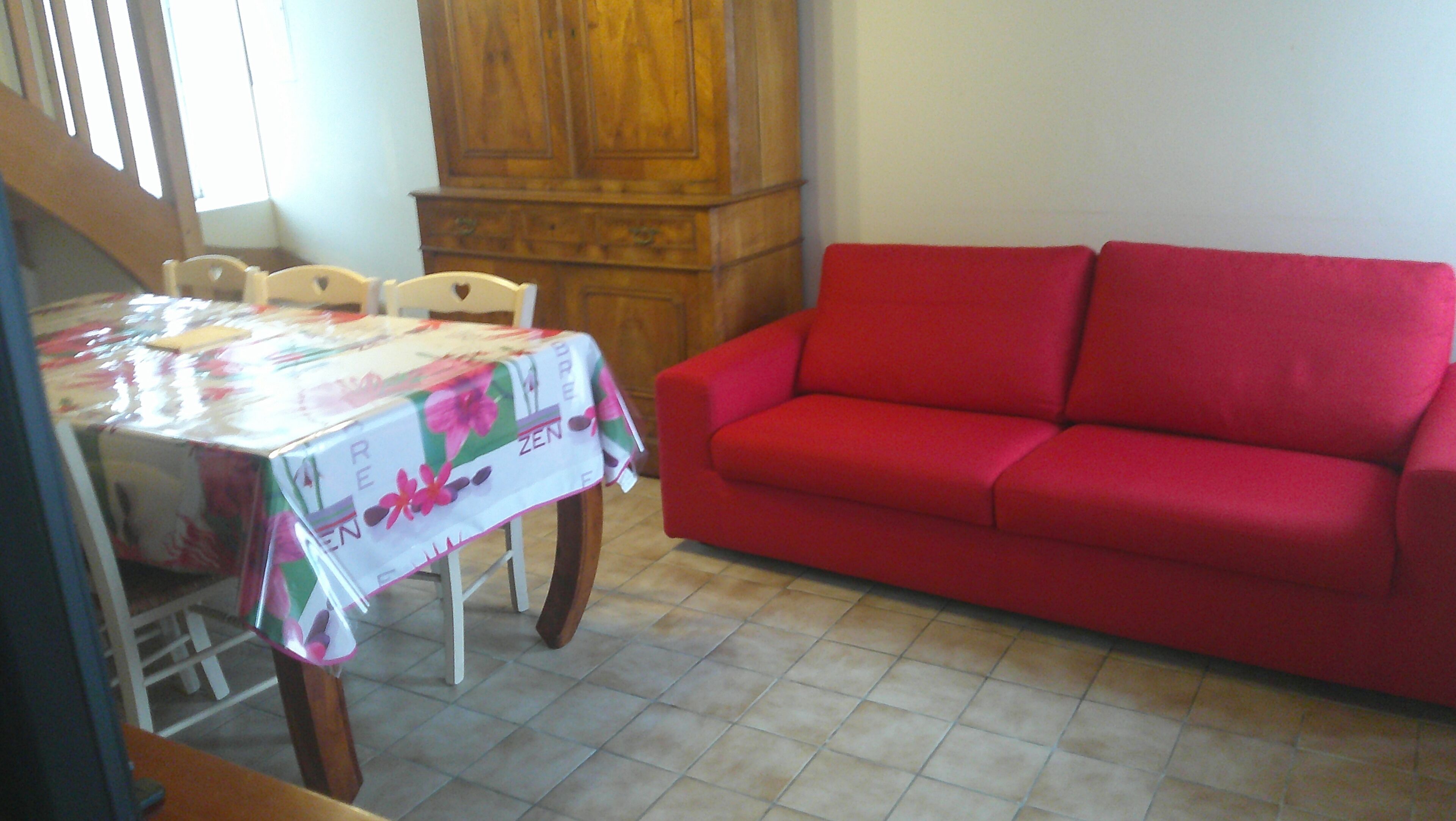 Un coin repas avec une table recouverte d’une nappe à motifs floraux, un canapé rouge et un meuble en bois.