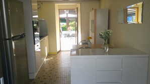 Una cocina con refrigerador, pileta y comedor, con un florero de flores.