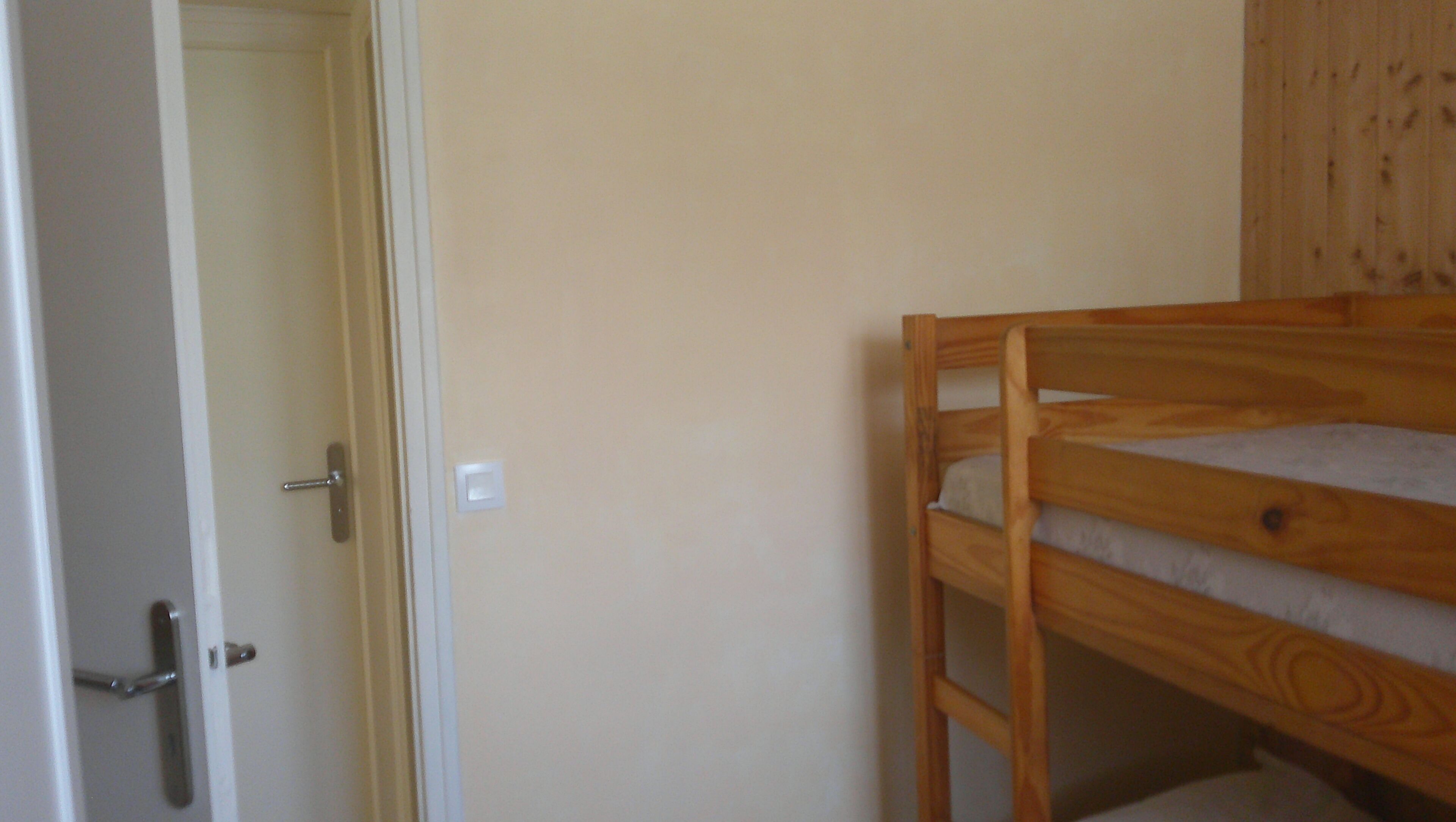 A room with a wooden bunk bed, a door with a handle, and a light switch on the wall.