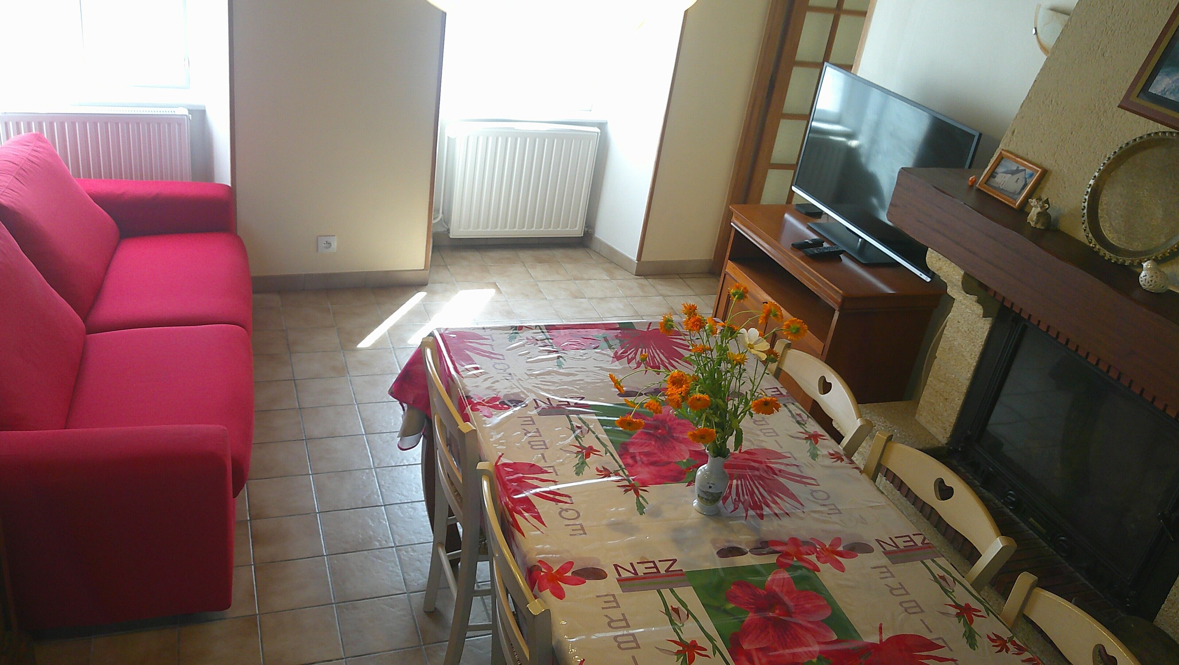 Una sala de estar con un sofá rojo, una mesa con mantel floreado, un televisor y una chimenea.