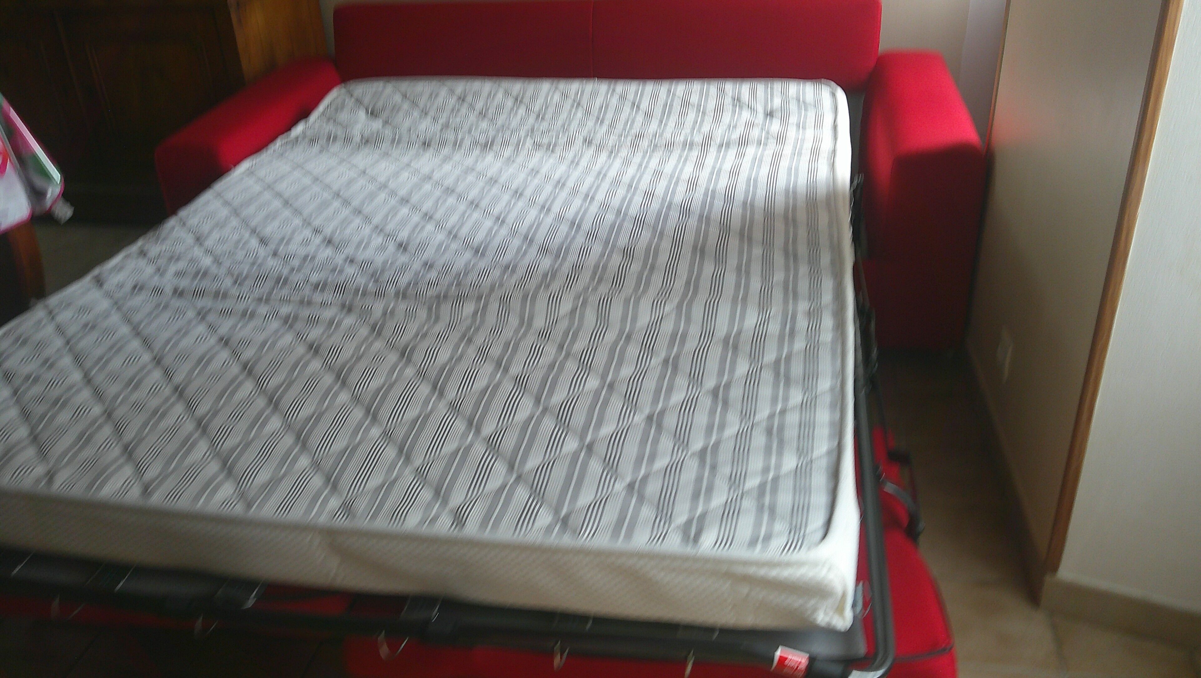 A bed with a patterned bedspread, a red headboard, and a red cushion.