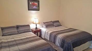 A room with two beds, a nightstand with a lamp, and a framed picture on the wall.