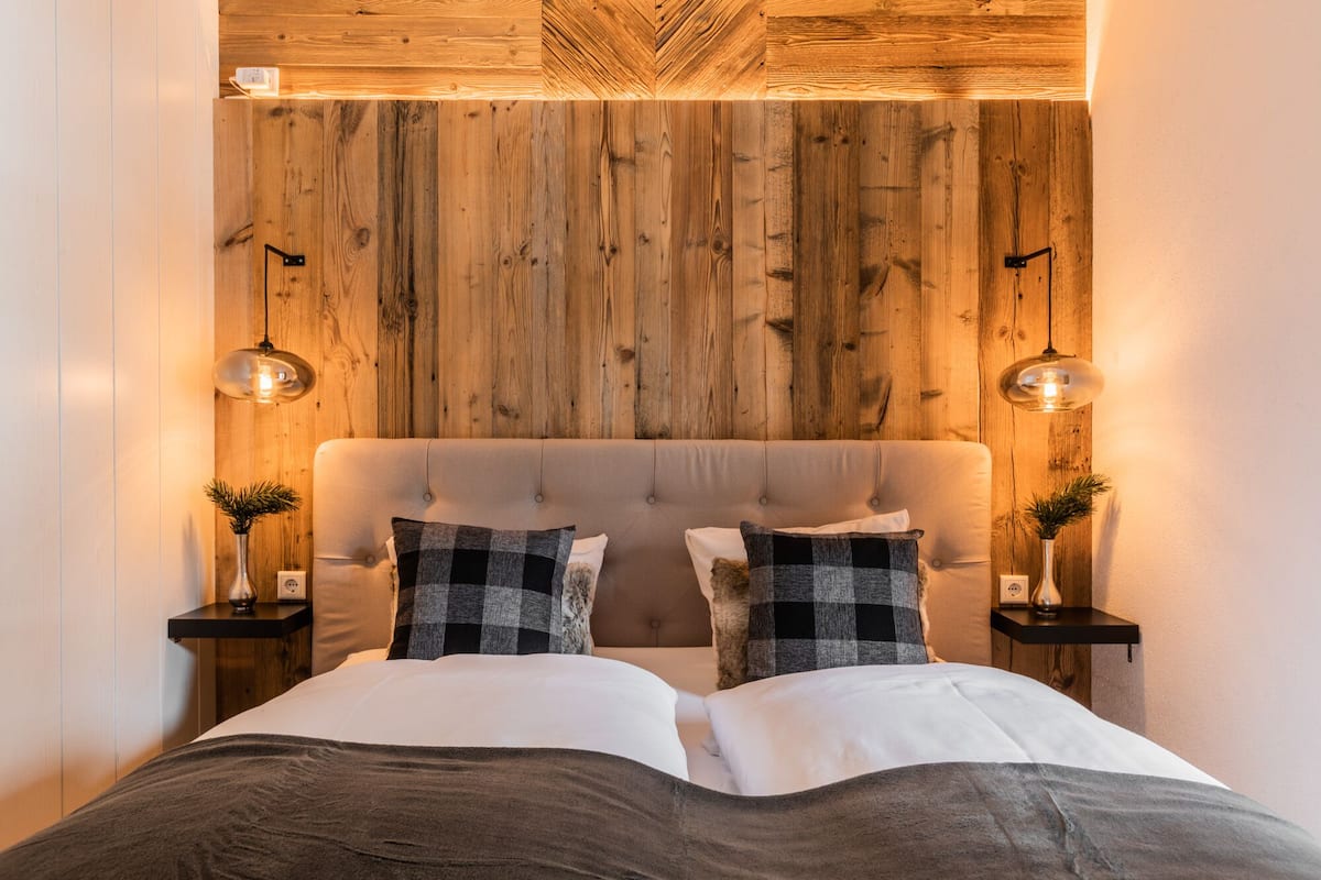 A bedroom with a wooden headboard, two bedside tables with lamps, and a bed with a grey blanket.