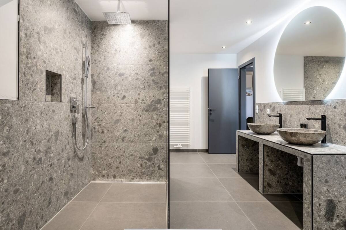 A modern bathroom with a glass-enclosed shower, granite countertops, and a large mirror.