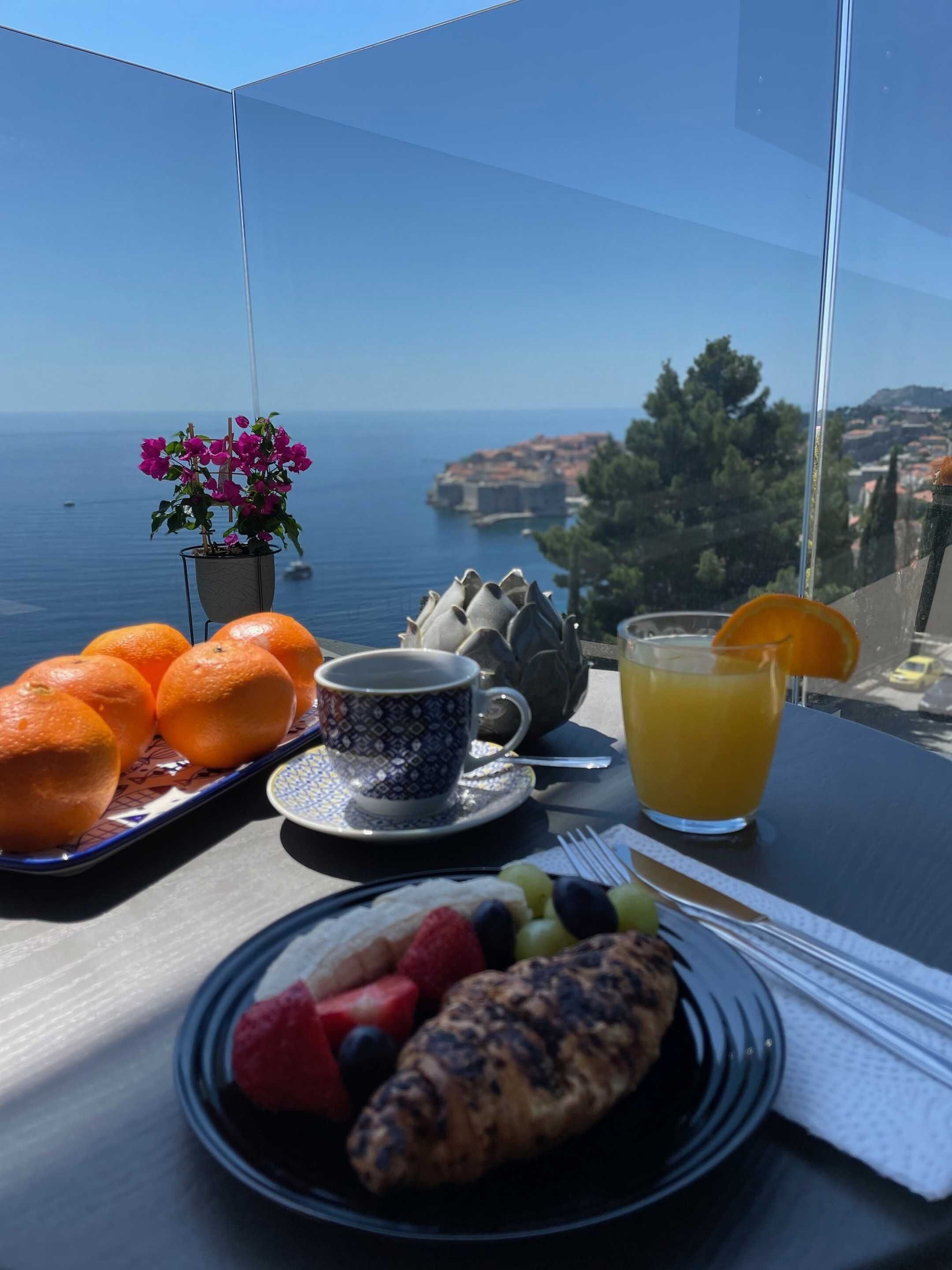 Una mesa con alimentos para el desayuno, incluyendo naranjas, una taza de café, un vaso de zumo de naranja y un plato con frutas y un croissant.