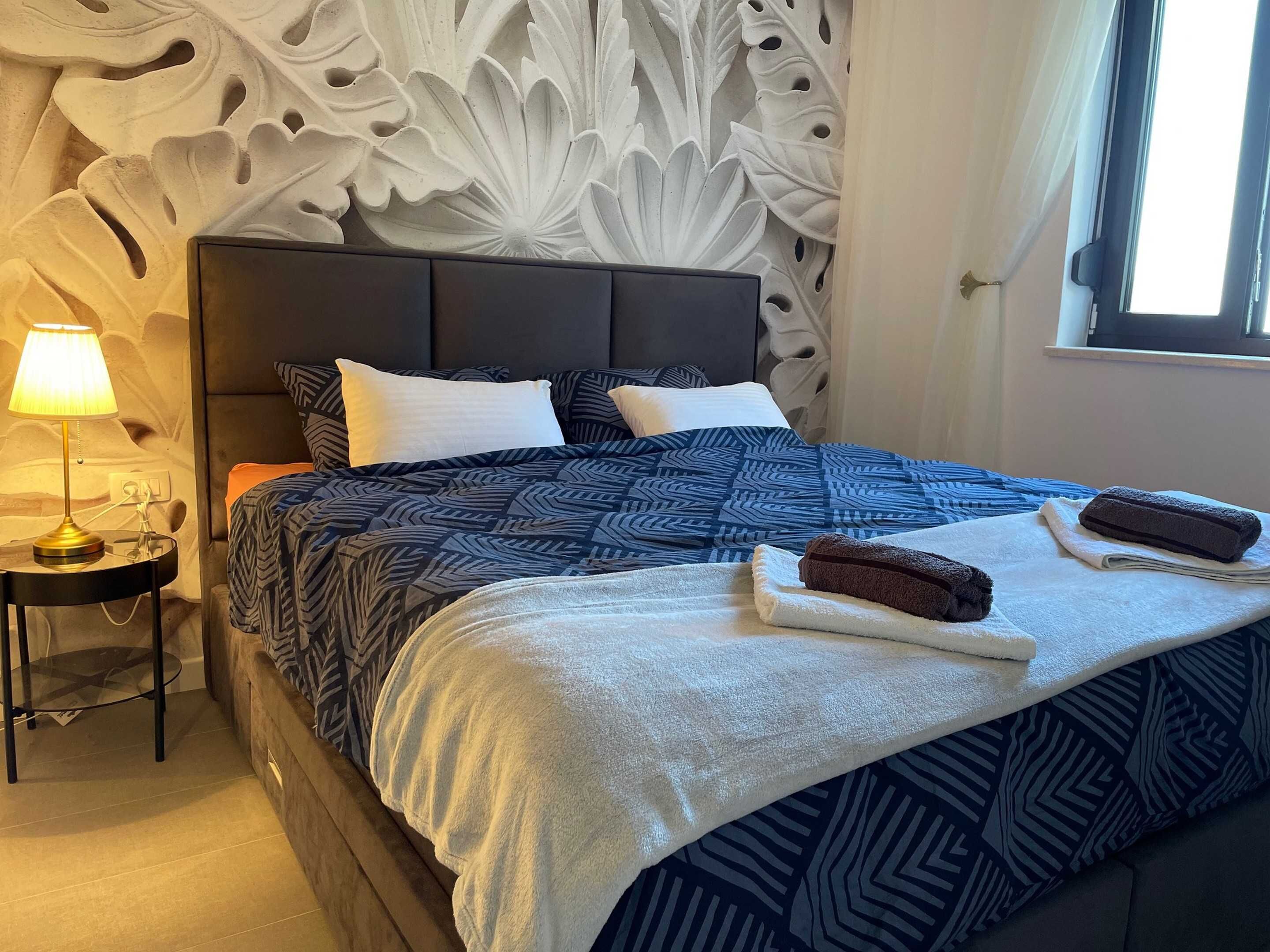 Una cama bien hecha con ropa de cama estampada, una lámpara de noche y un adorno en la pared.