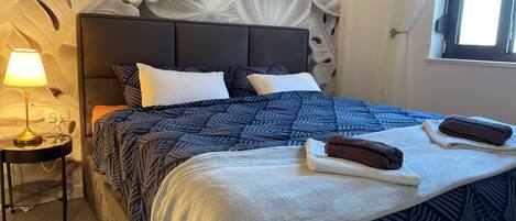 Una cama bien hecha con ropa de cama estampada, una lámpara de noche y un adorno en la pared.