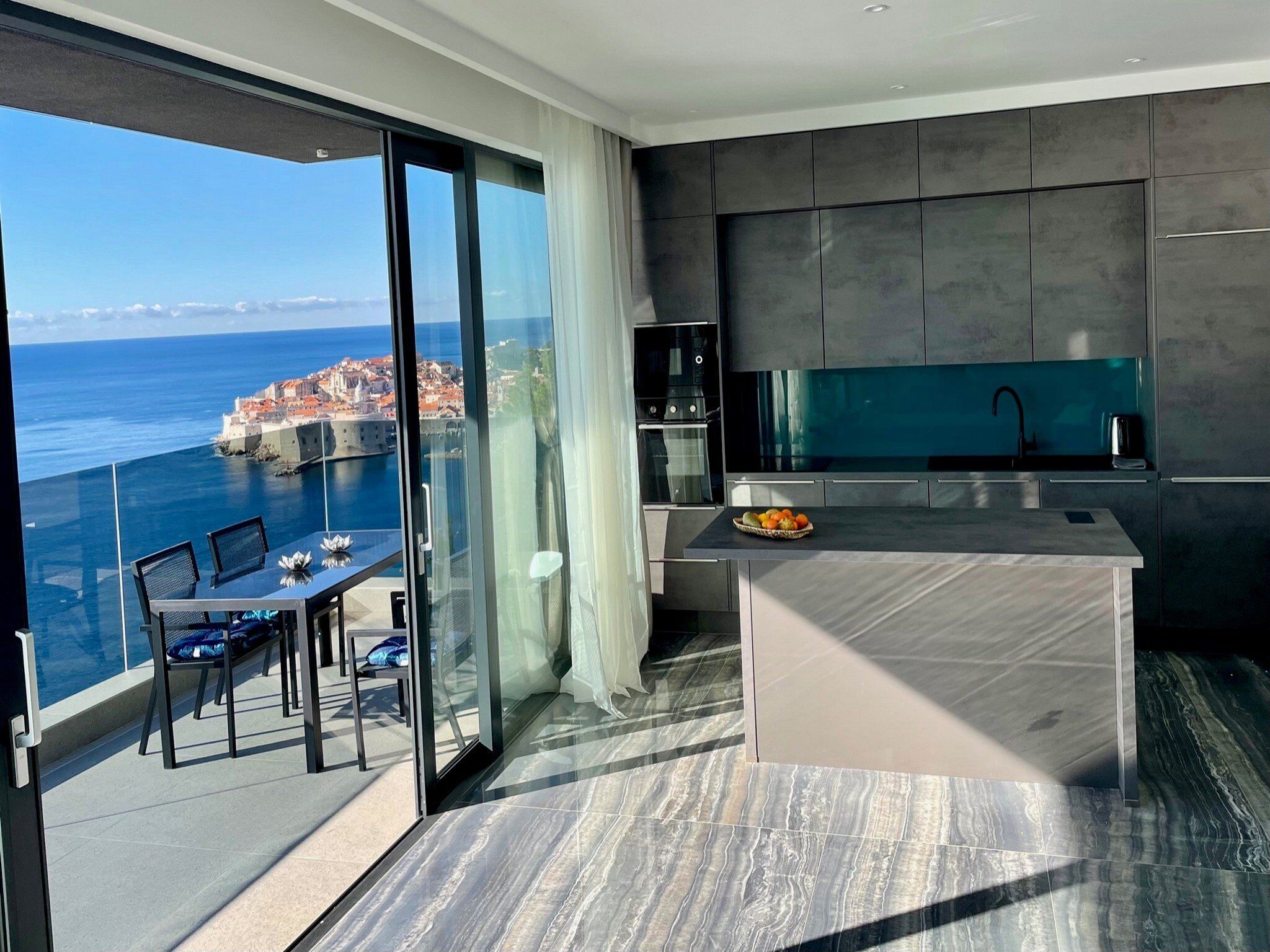 A modern kitchen with a view of the sea, a dining area with a table and chairs, and a large sliding glass door.