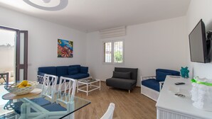 Una sala de estar moderna con una mesa de comedor de vidrio, sofás azules, una mesa de centro blanca y un ventanal grande.