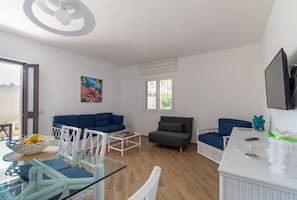 Un salon moderne avec une table à manger en verre, des canapés bleus, une table basse blanche et une grande fenêtre.