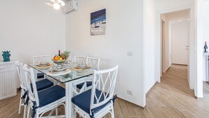 Un comedor con una mesa de vidrio, sillas blancas y un cuadro en la pared.