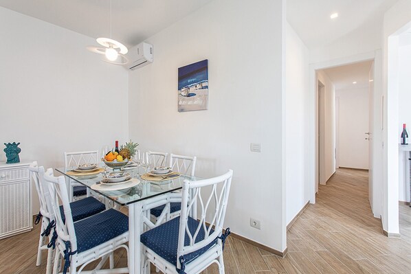 A dining area with a glass table, white chairs, and a painting on the wall.