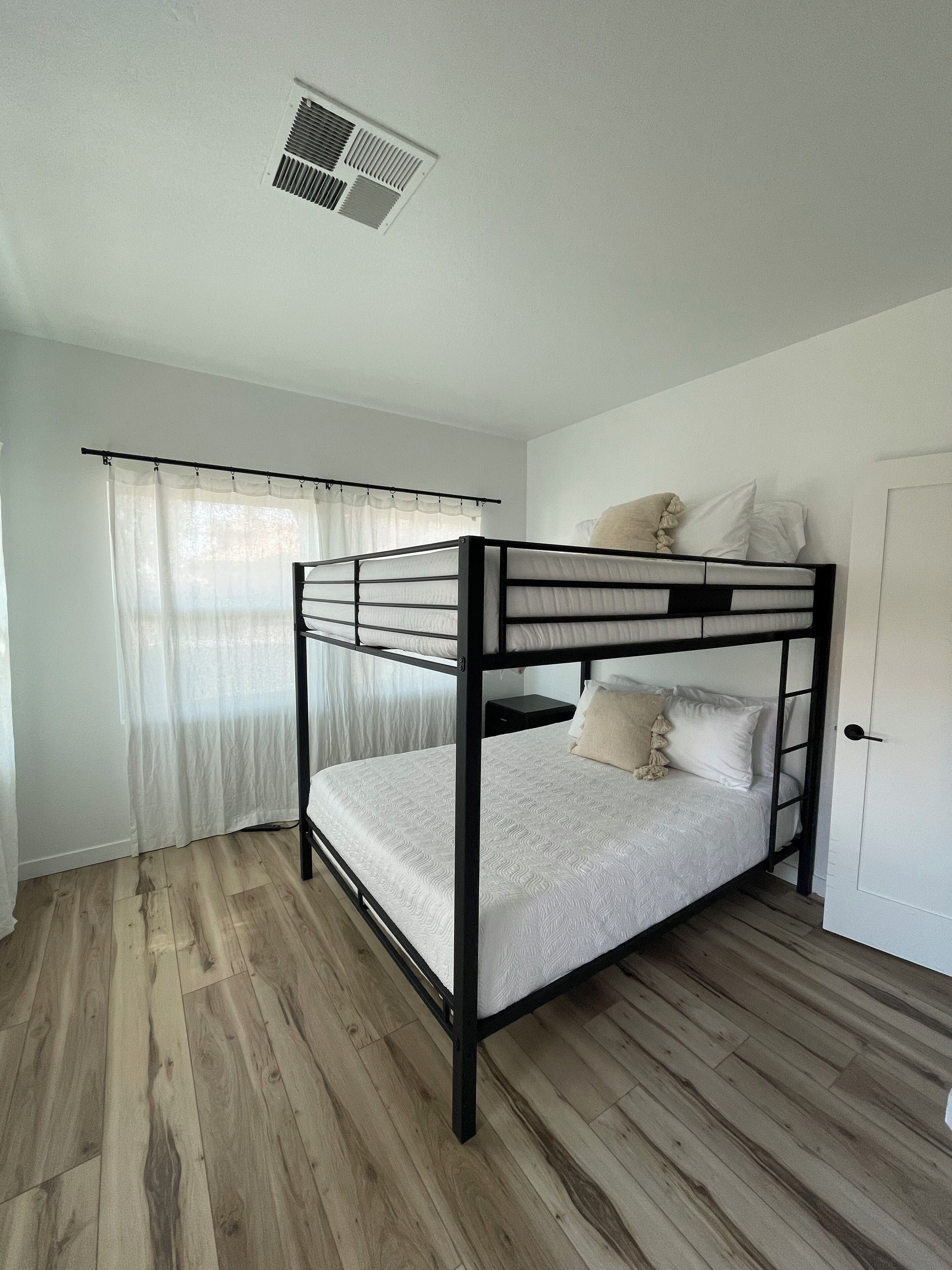 A bunk bed with a headboard, a curtained window, and a door.