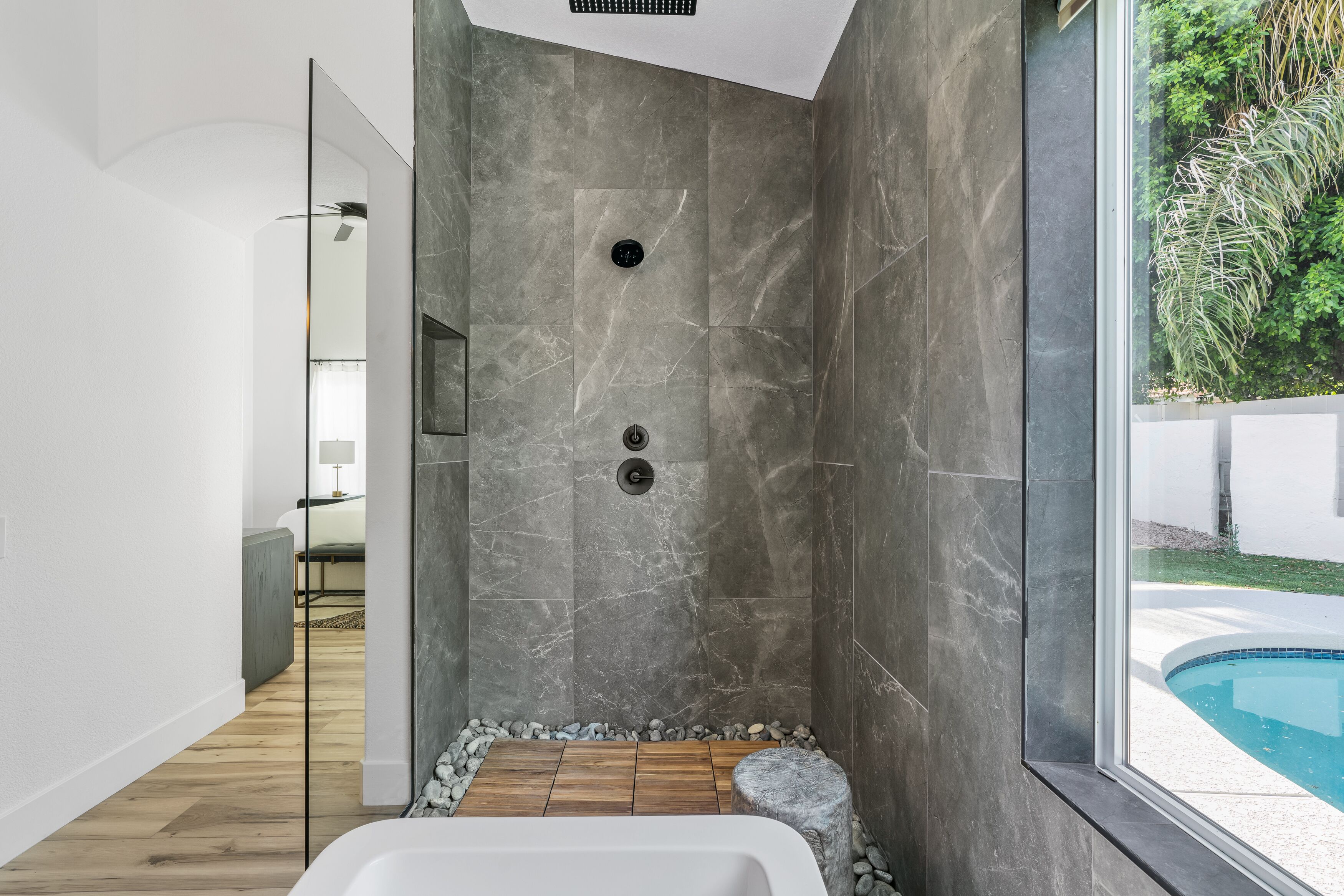 A modern bathroom with a walk-in shower, a bathtub, and a view of a swimming pool.