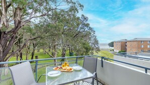 Ein Balkon mit Frühstückstisch, mit Blick auf eine Rasenfläche und ein Gebäude.
