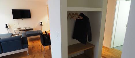Una sala de estar moderna con un sofá, televisor y mueble de entretenimiento. Un pasillo conduce a un dormitorio con armario y puerta.