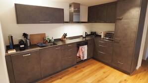 Una cocina moderna con armarios oscuros, una encimera de madera y un lavamanos de acero inoxidable.