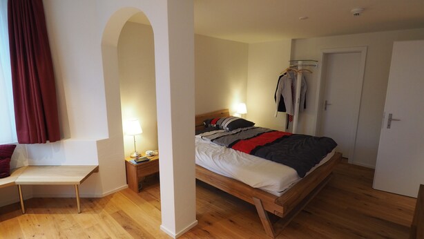Un dormitorio con cama de madera, una mesita de noche con lámpara, una silla y un armario.