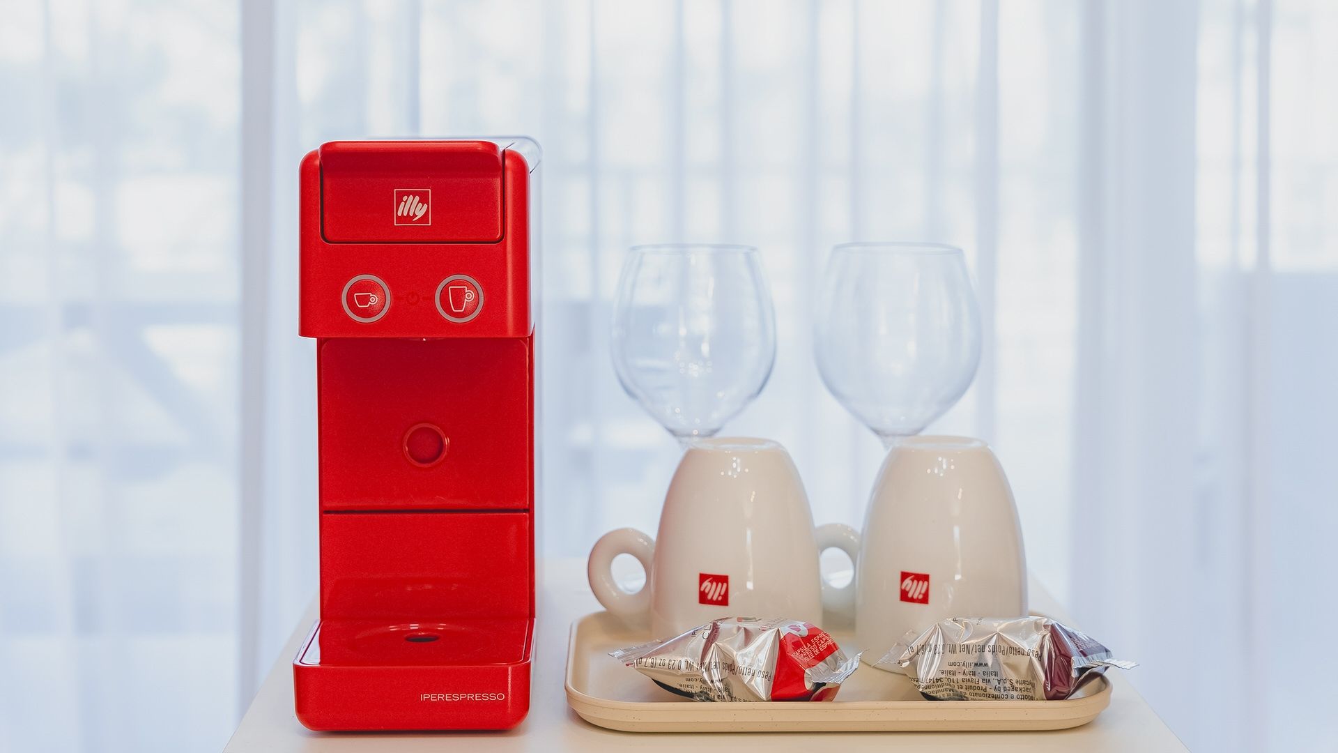Una cafetera roja con dos tazas y una bandeja de cápsulas de café.