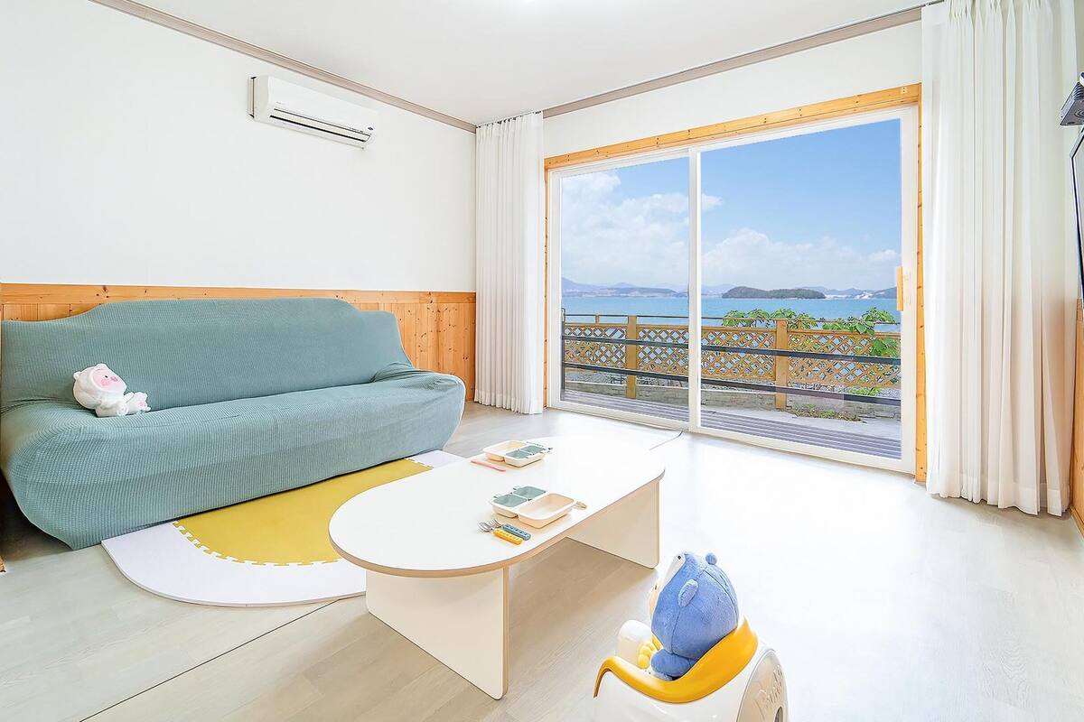 A modern room with a green sofa, a small table, and a view of the sea through large windows.