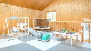 A room with wooden walls, a play area with a slide, a trampoline, and a table with toys. - Yeosu Hi Mom Kids Family Pension Gold (Yeosu)