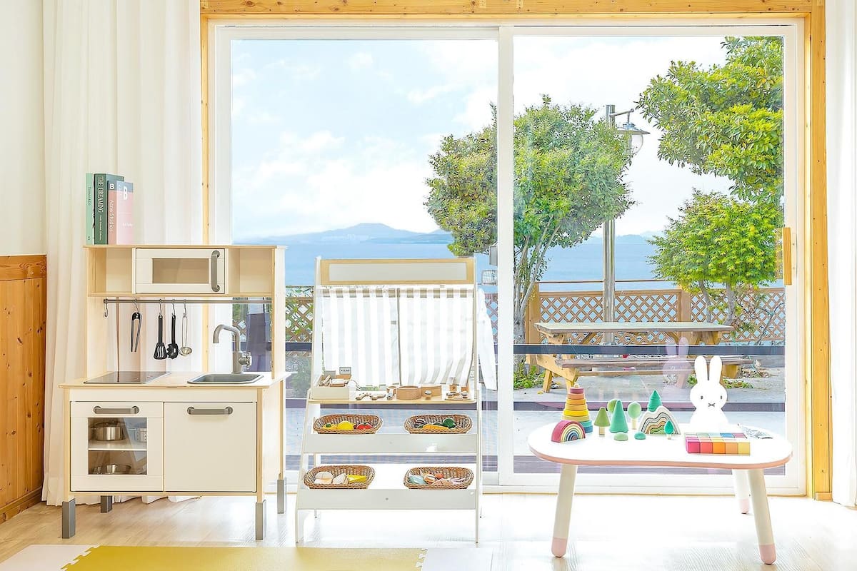 A bright kitchen with a view of the sea, a dining area with a table and chairs, and a small play area with toys.