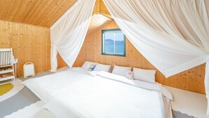 A bedroom with a large bed, wooden walls, and a window with a view of the sea. - Yeosu Hi Mom Kids Family Pension Gold (Yeosu)