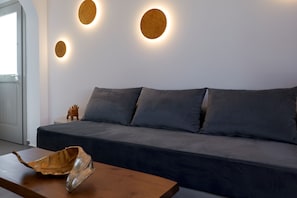 A modern living room with a dark grey sofa, a wooden coffee table, and three wall-mounted round light fixtures. - Mountain and Sea Suites (Santorini)