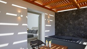 A modern outdoor seating area with a stone wall, a wooden table, and a chair. - Mountain and Sea Suites (Santorini)