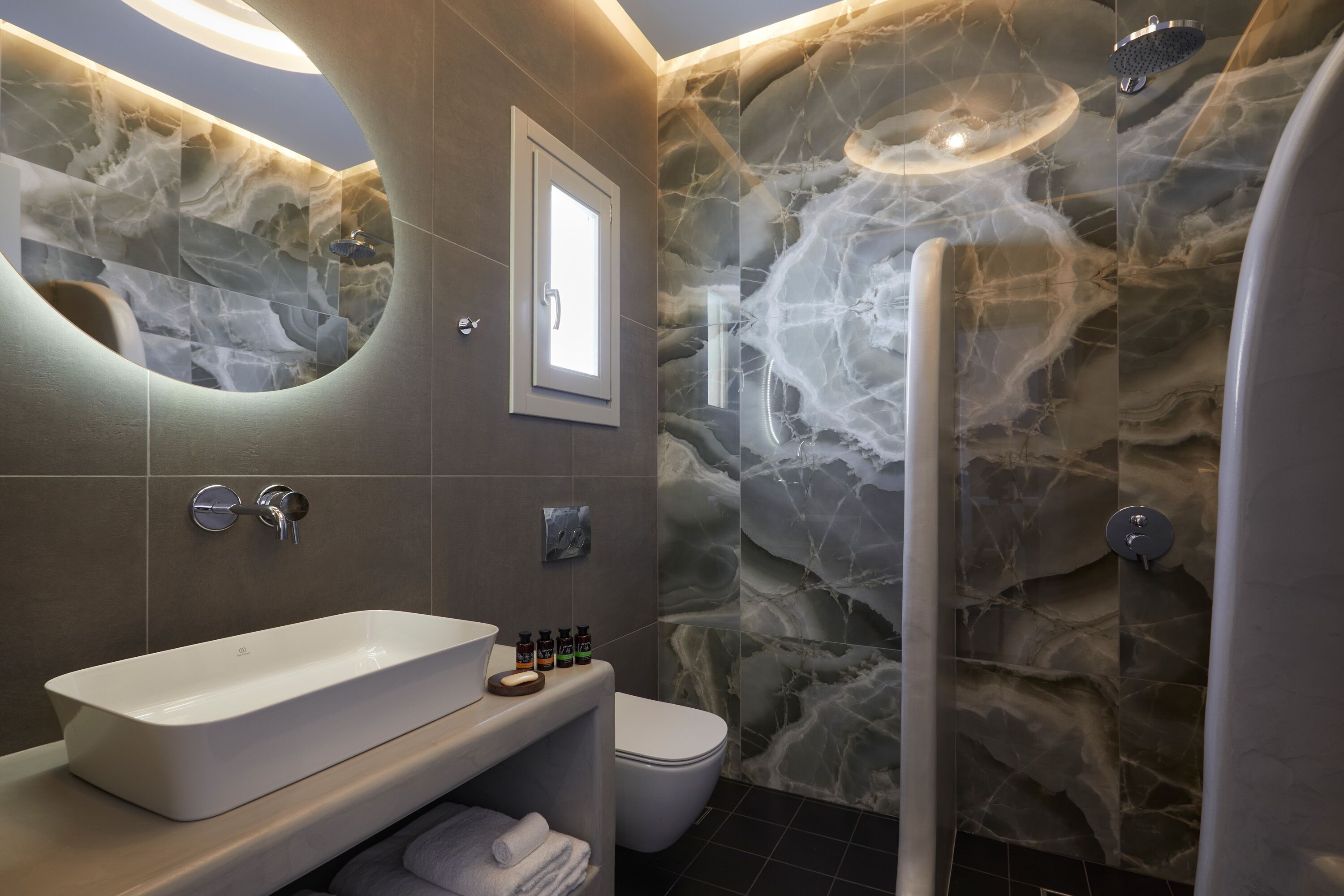 A modern bathroom with a marble wall, a freestanding bathtub, a toilet, and a shower.