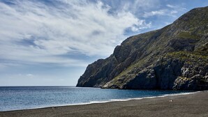 A coastal landscape with a rocky cliff and a beach. - Mountain and Sea Suites (Santorini)