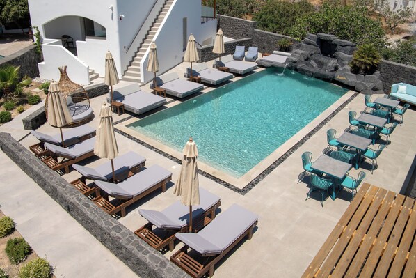 A pool area with lounge chairs, umbrellas, and a wooden deck. - Mountain and Sea Suites (Santorini)