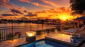 Ein Pool mit Liegestühlen, eine Whirlwanne und Blick auf einen Sonnenuntergang über dem Wasser.