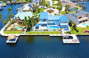 A large blue house with a swimming pool, docked boats, and a marina.
