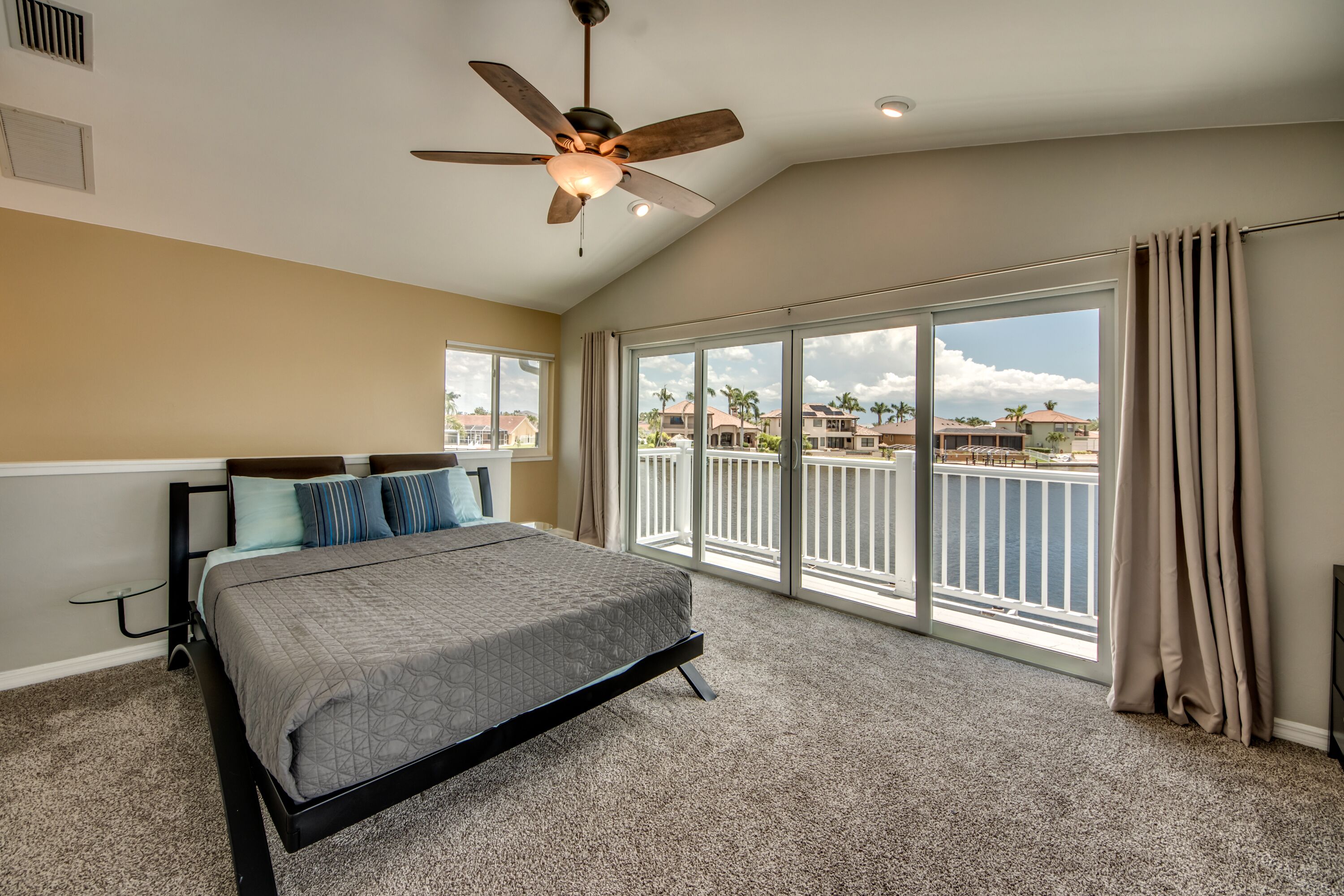 A bedroom with a bed, a ceiling fan, large windows, and a view of the ocean.