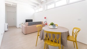 Une pièce moderne et bien éclairée, avec une table ronde, des chaises jaunes, un canapé beige et une petite plante posée sur la table.