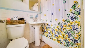 A bathroom with a toilet, sink, and shower curtain with a floral pattern. - 🏳️‍🌈 #1 Walk to Wilton Drive (fort lauderdale)