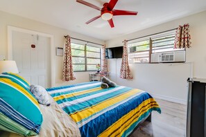 A hotel room with a bed, a desk, a TV, and a ceiling fan.