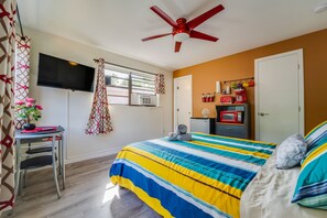 A hotel room with a bed, a TV, a ceiling fan, a window, and a kitchenette.