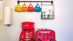 Une cuisine avec une machine à café rouge, un grille-pain rouge et des tasses colorées suspendues à un porte-tasses.
