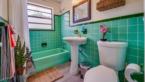 Une salle de bain avec des carreaux verts, une baignoire, un lavabo et des toilettes.